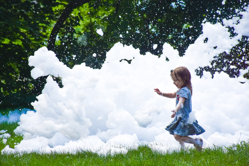 A young girl running through a pile of foam outside.